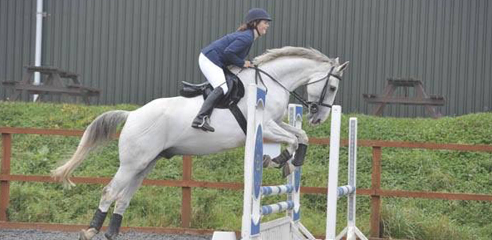 Grey horse jumping a show jump in an arena