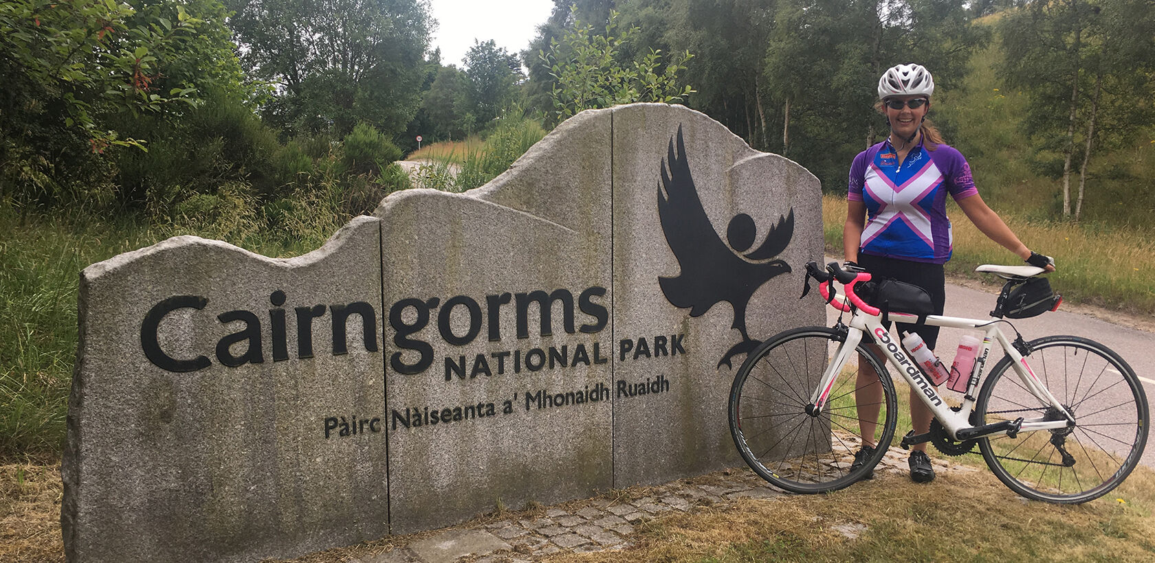 Female cyclist stood with bike next to Cairngorms sign